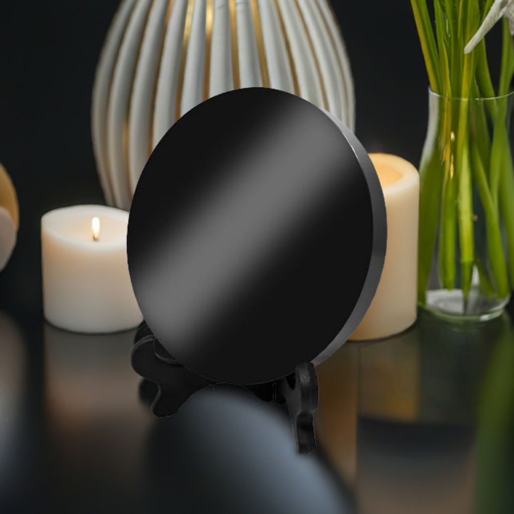 Black obsidian scrying mirror displayed on a stand, surrounded by lit candles and a vase of flowers, creating a mystical and calming atmosphere ideal for meditation and spiritual practices.